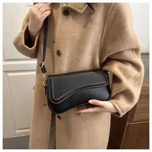 Detail of black leather crossbody bag with irregular saddle flap and gold hardware