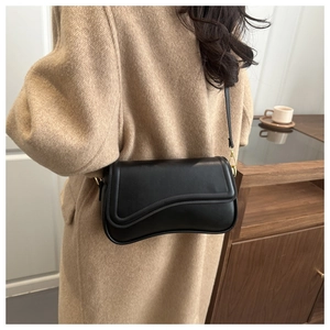 Detail of a matte black leather crossbody bag featuring a unique wavy flap and gold hardware
