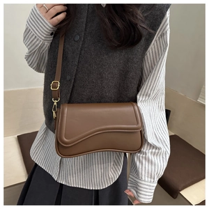 Brown leather crossbody bag detail featuring asymmetrical wavy flap and golden buckle