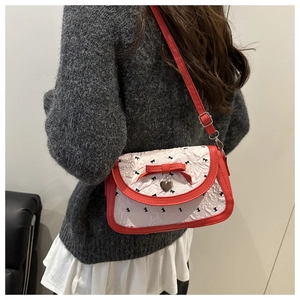 Détail du sac blanc texturé avec nœud rouge et pendentif cœur porté par le mannequin