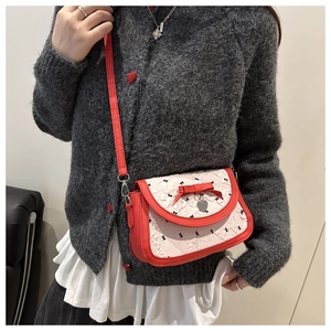 Détail du nœud rouge et pendentif cœur sur sac bandoulière texturé avec motifs de papillons