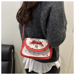 Detail of white pleated crossbody bag with red piping and heart-shaped metal pendant