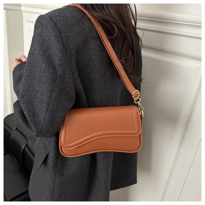 Detail of caramel shoulder bag with wave flap and gold hardware on grey blazer