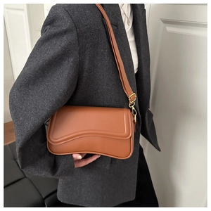 Close-up of brown leather crossbody bag with wave-edge flap on model in grey suit