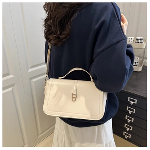 Detail of off-white leather shoulder bag featuring a gold buckle and wide strap
