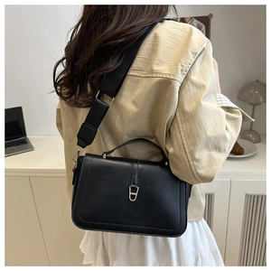 Détail d'un sac bandoulière en cuir noir avec large sangle en tissu et boucle dorée