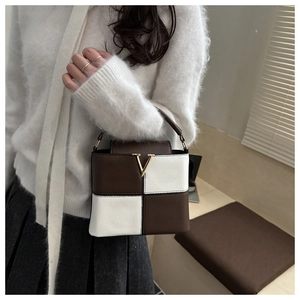 Fashionable brown and beige patchwork handbag with gold V-shaped buckle on model