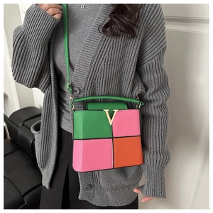 Detail of color-block leather crossbody bag with V-shaped gold logo and green handle