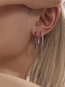 Detail of titanium steel earrings with blue and white cubic zirconia on a model ear