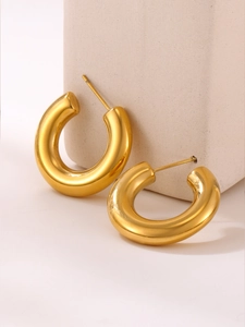 Vue macro de boucles d'oreilles C épaisses plaquées or sur un support en pierre