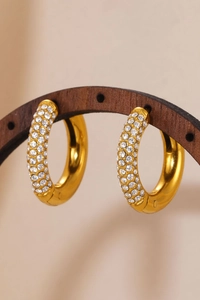Close-up of gold hoop earrings with multi-row pavé zircon on dark wood stand