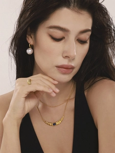 Détail de colliers dorés superposés avec pendentif lapis et boucles d'oreilles perles