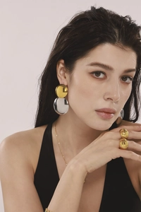 Gros plan de boucles d'oreilles bicolores et de bagues texturées sur un mannequin