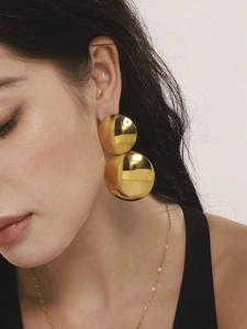 Gros plan sur des boucles d'oreilles doubles sphères dorées avec texture métallique polie