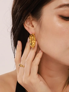 Close-up of golden scale texture hoop earrings and minimalist ring on a model