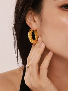 Detailed close-up of 18k gold plated U-shaped earrings with scale texture on a model