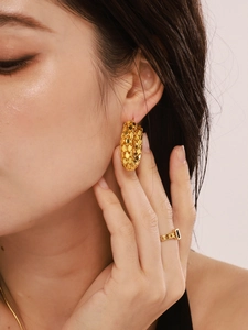 Close-up of golden hollow fish scale earrings and matching ring on female model