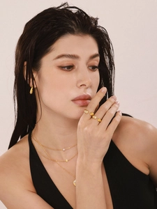 Close-up of a model wearing layered gold necklaces, chunky rings, and hoop earrings