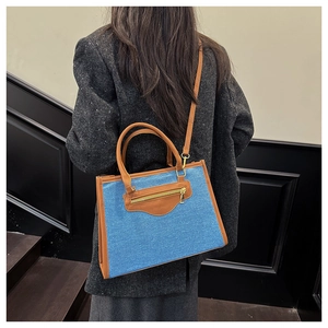 Detalle del bolso tote de mezclilla azul con asas de cuero marrón sobre una chaqueta tweed