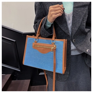 Detalle de bolso tote grande de mezclilla azul y cuero marrón con una modelo