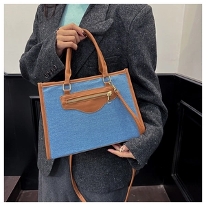 Detalle del bolso tote de mezclilla azul con cuero marrón y bolsillo frontal con cremallera