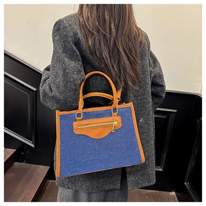 Detalle del bolso tote de mezclilla con ribete de cuero llevado por modelo en abrigo de tweed