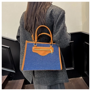 Detalle de bolso tote denim azul con asas de cuero marrón y detalles de cremallera dorada
