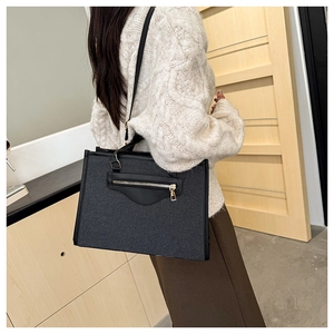 Detalle de un bolso tote negro grande con cremallera dorada y textura de lona y cuero