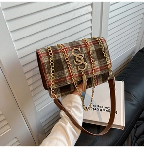 Detail of red and brown plaid crossbody bag with golden S-buckle and tassel accent