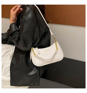 Detail of white ostrich-pattern underarm bag with gold chain on model in leather jacket