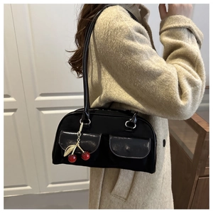 Detail of black Boston bag featuring glossy flap pockets and a cherry charm decoration