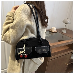 Detail of black Boston bag with glossy shoulder straps and red cherry charm accessory