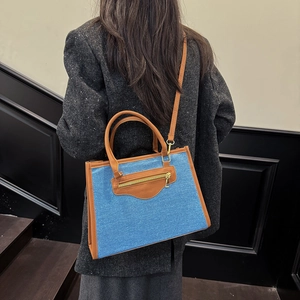 Bolso tote de denim azul y cuero marrón con asa superior y detalle de cremallera dorada
