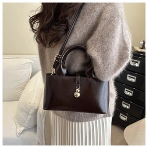 Détail d'un sac à main marron foncé avec charm sphère dorée et bandoulière réglable