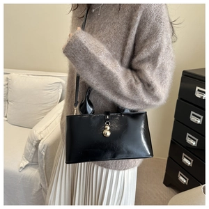 Détail du sac baguette noir minimaliste avec élégant pendentif à double sphère dorée