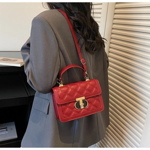 Detail of red quilted crossbody bag with golden T-lock worn by model in gray suit