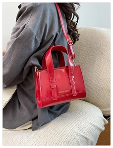 Close-up of red patent leather handbag with adjustable strap and fashion gold lettering