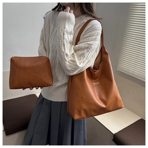 Close-up of brown leather tote and matching pouch set worn with white knit sweater