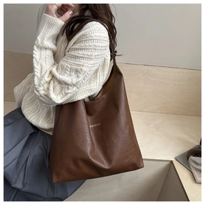Detail van bruine tote bag met litchi-patroon en gouden FASHION-belettering op leer