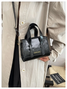 Detail of glossy black PU leather handbag featuring elegant gold lettering and dual handles