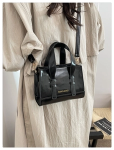 Detail view of mini black glossy leather handbag with gold crossbody strap on a model
