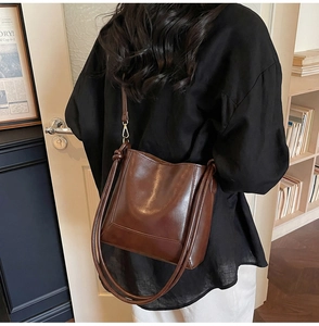 Detail view of large brown glossy leather bucket bag worn by model in cozy interior