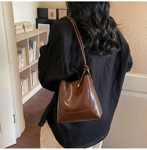 Model wearing a brown glossy leather bucket tote bag against a vintage bookshelf background