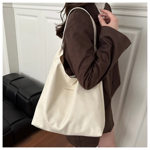 Detail of cream white tote bag with ruched leather texture and golden Fashion text