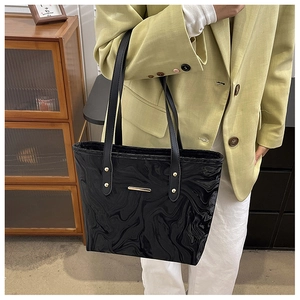 Glossy black tote bag with water ripple texture and gold metal bar on green blazer