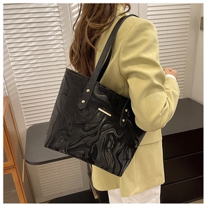 Detail of black marble textured tote bag with gold metal accents on a stylish model