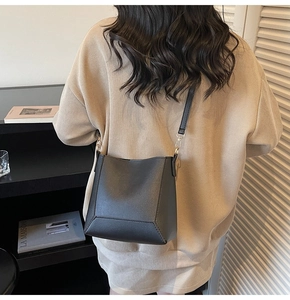 Detail of a minimalist black bucket bag with square bottom and gold metal buckle hardware
