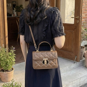 Brown quilted crossbody bag with golden T-clasp carried by a model in a cafe setting