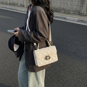 Beige quilted crossbody bag with golden twist lock and top handle in outdoor street setting