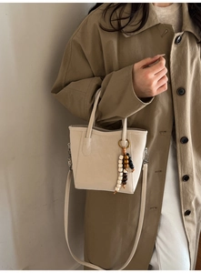 Detail of cream leather bucket bag with wooden bead charm and long shoulder strap
